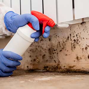 worker with gloves and protective suit removing mold under a heating battery